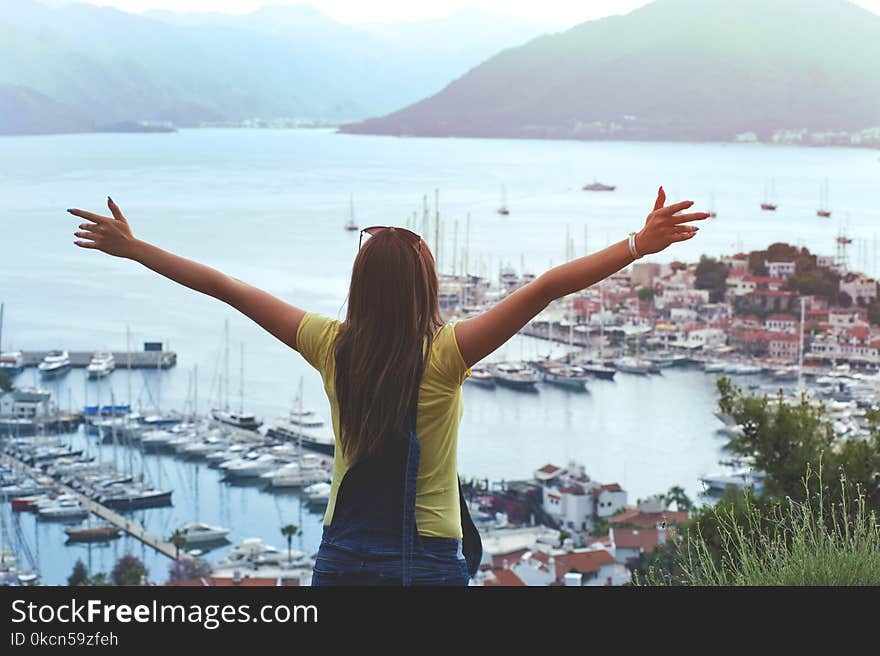 Woman Raising Her Hands Facing Cityscape Near Body of Water