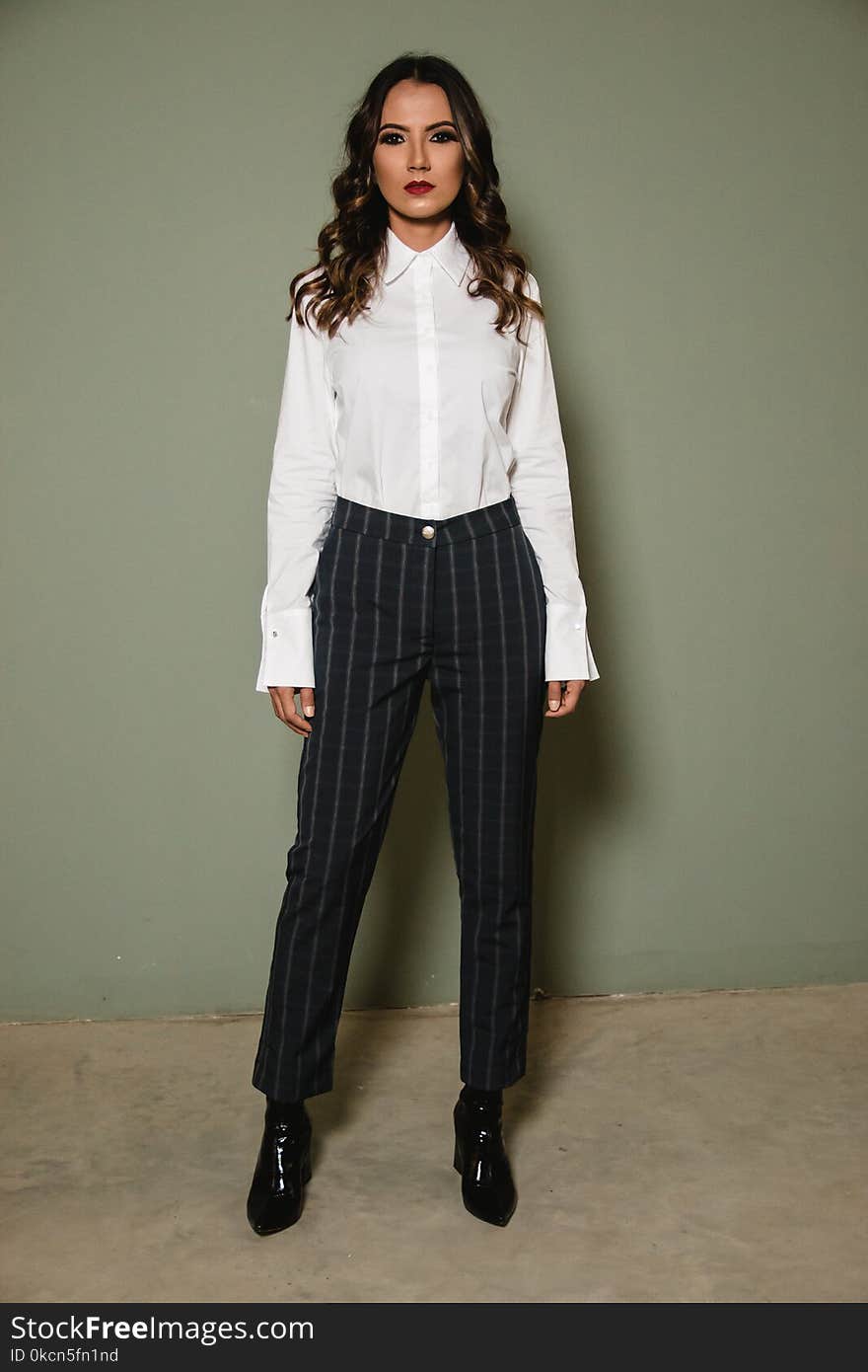 Woman Posing in White Dress Shirt and Black Pants Standing Against Gray Wall