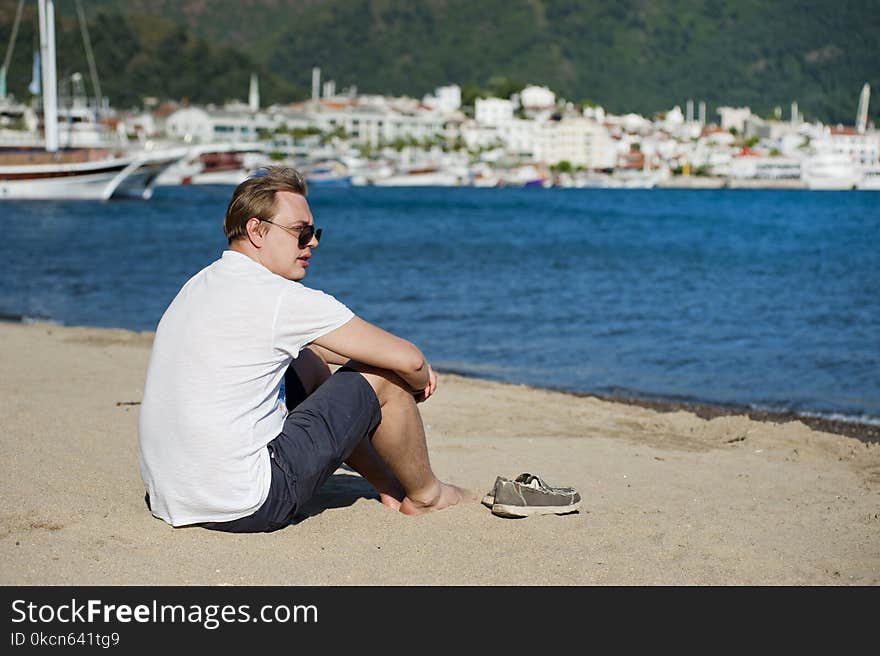 Photo of Man in White Shirt and Blue Short Sitting on Seashore