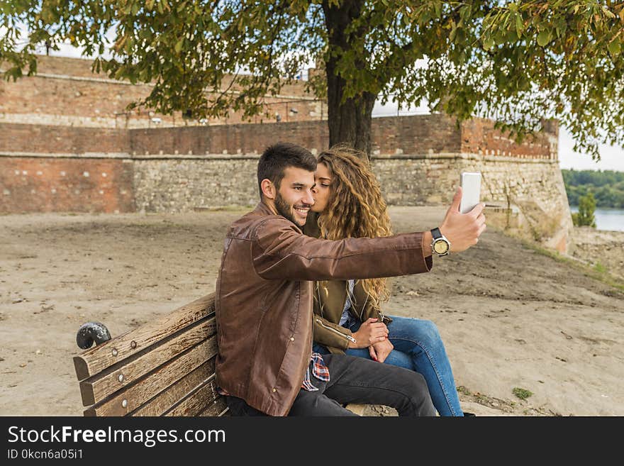 Woman And Man Sitting On Brown Wooden Bench Kissing