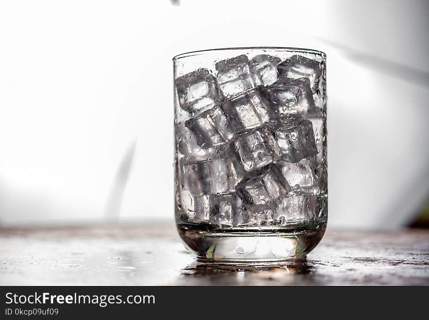 Glass Of Ice Cube On Wooden Table And Light Blurred Background