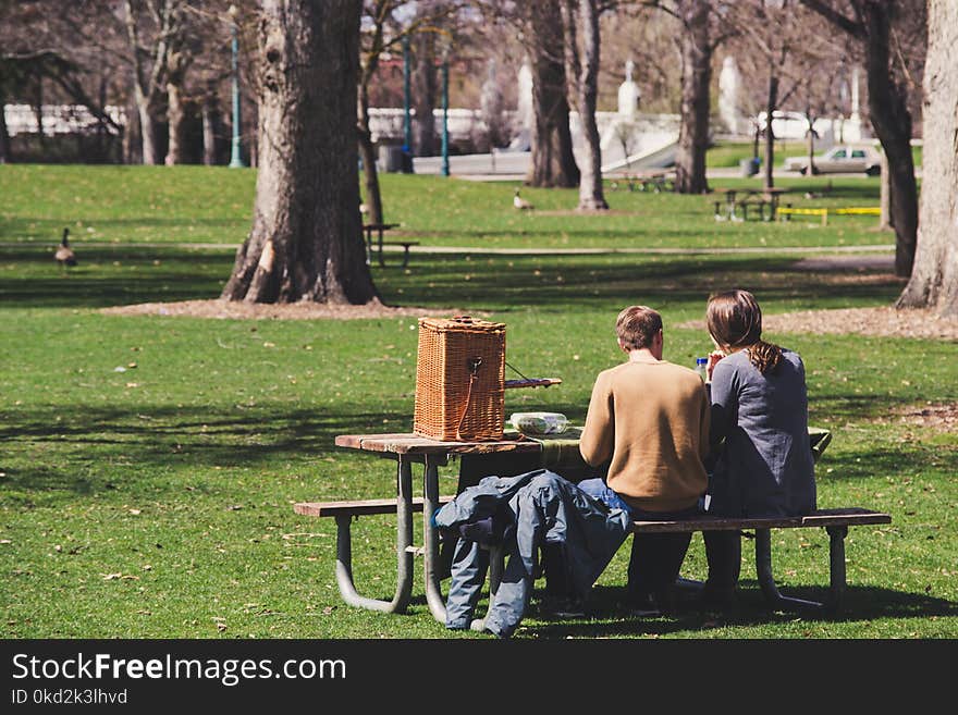 Man and Woman Sitting on Brown Wooden Picnic Table