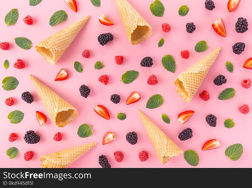 From above view of empty waffle cones in arrangement with mixed berries and mint leaves on pink. From above view of empty waffle cones in arrangement with mixed berries and mint leaves on pink.