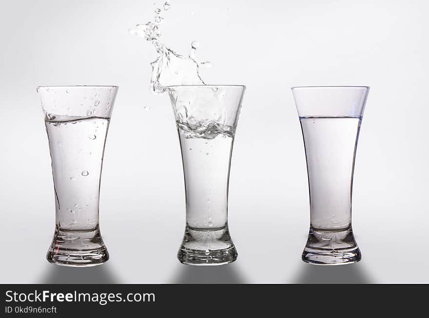 Three glasses and a splash of water on a gray background