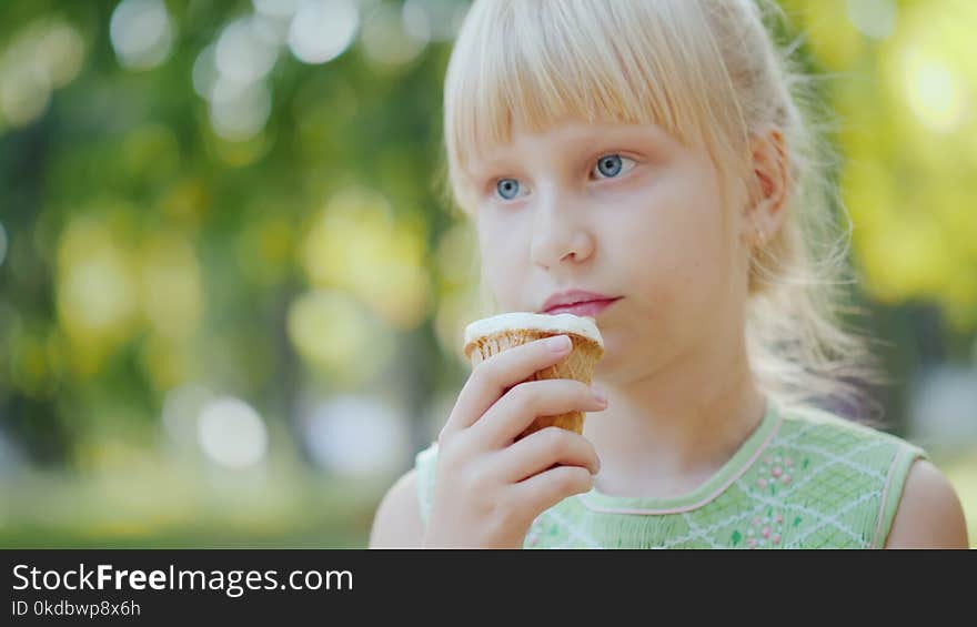 Thoughtful girl 6 years old is eating ice cream in the park. Holiday in summer and vacations. 4K 10 bit video