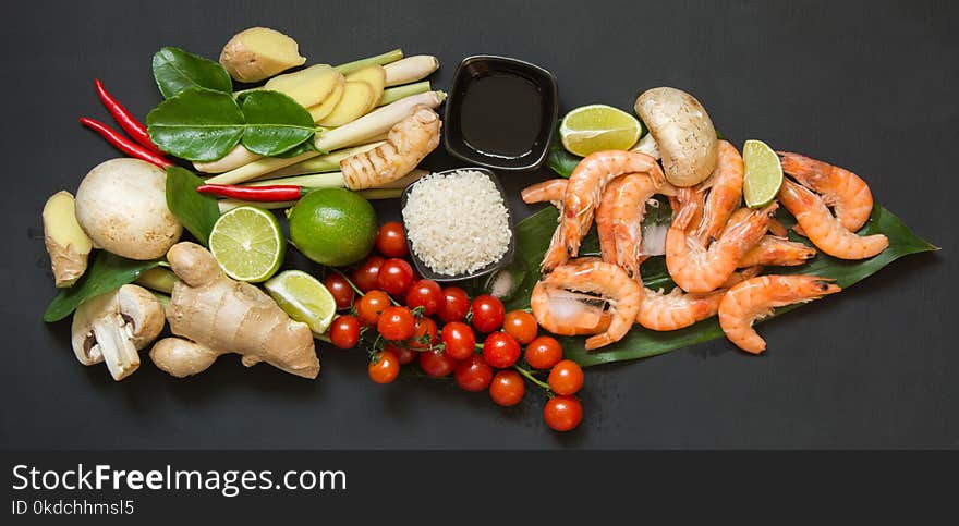 Special ingredients for popular Thai spicy soup Tom-yum kung lime, galangal, red chili, cherry tomato, lemongrass and kaffir lime leaf on black table with copy space. Top view.