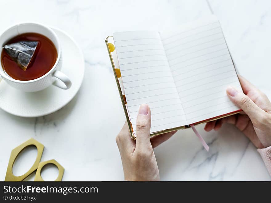 Person Opened a Book Near White Ceramic Cup Filled With Coffee