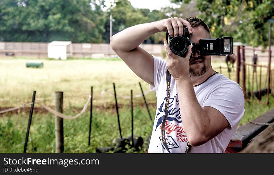 Man Holding Dslr Camera While Standing Near Fence