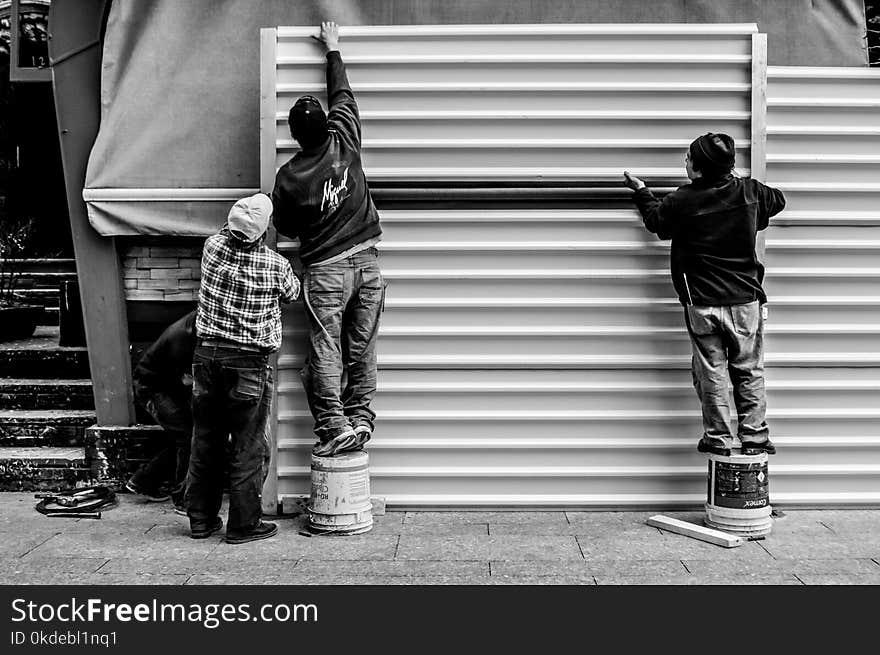 Grayscale Photo of Three Men Arranging Metal Wall