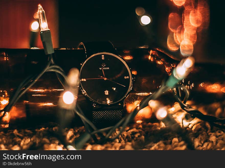 Round Silver-colored Analog Watch With Black Band Surrounded With String Lights Selective Focus Photography