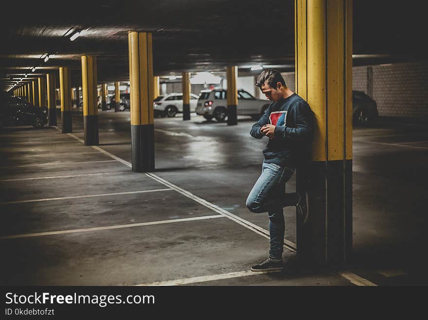 Man in Dark-gray Crew-neck Sweater Standing Leaning to Post in Parking Lot