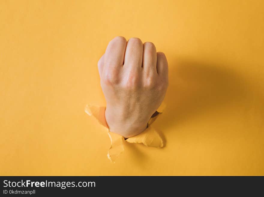 Female Fist Punching Through A Paper, Isolated On A Yellow Background.