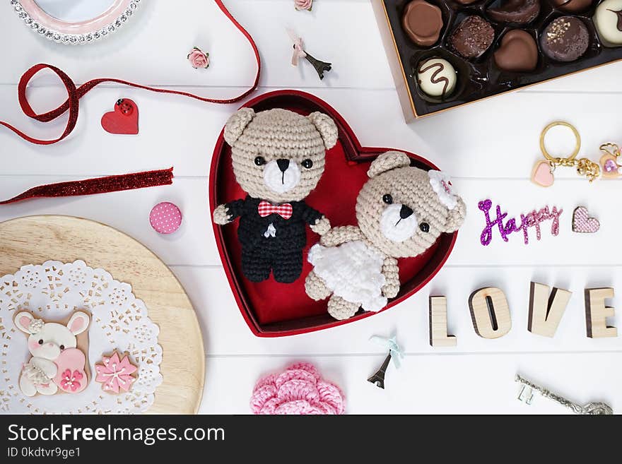 Happy anniversary present : bride and groom teddy bear crochet dolls or amigurumi, handmade bunny cookies and a box of chocolate on the white wooden board. Romantic Valentines gift. Selective focus.