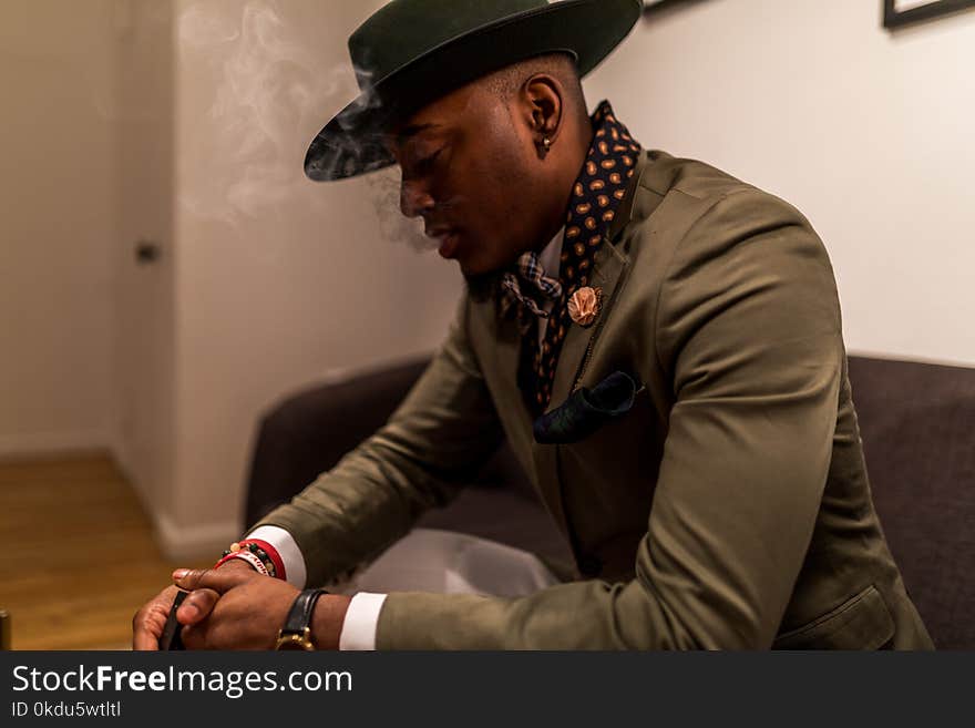 Man in Green Blazer With Cap Sitting on Black Sofa