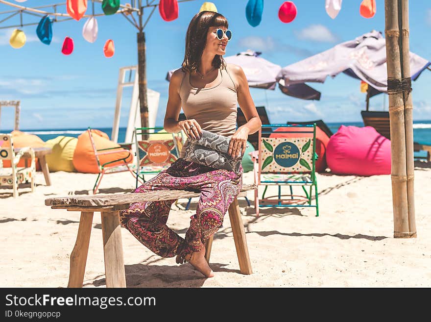 Woman Wearing Gray Tank Top Holding Gray and Black Clutch Sitting on Bench