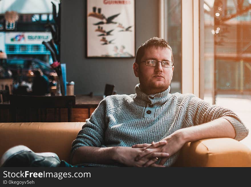 Man Wearing Gray Knitted Sweater Sitting on Brown Fabric Sofa