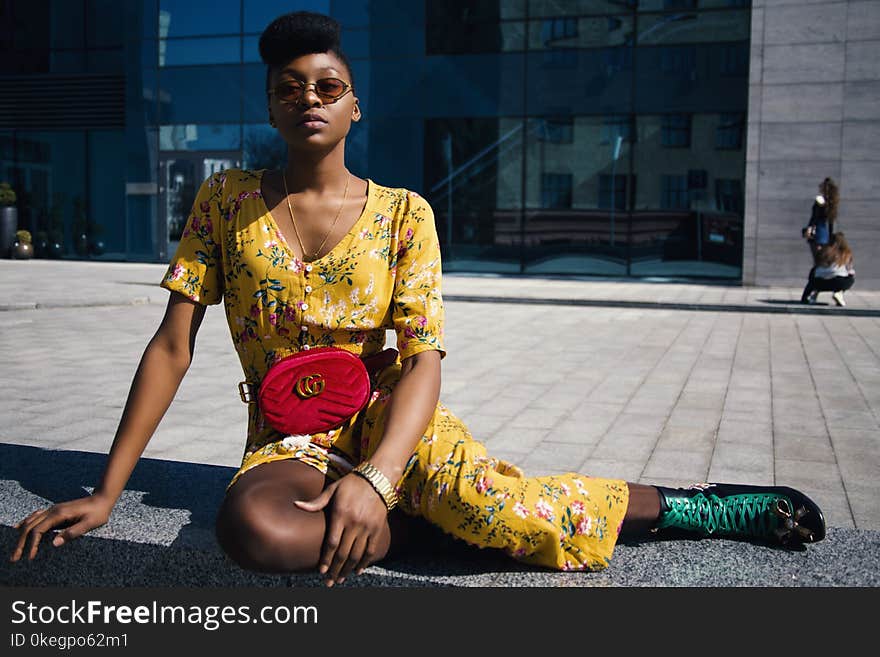 Woman in Yellow Floral Jumpsuit Sitting on Concrete Floor