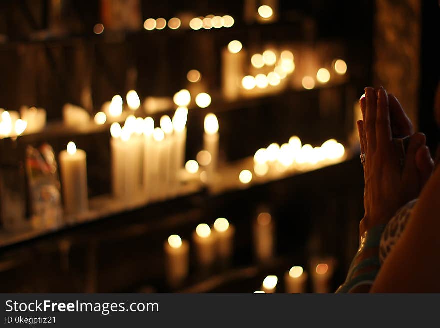 Close Up Photograph of Person Praying in Front Lined Candles