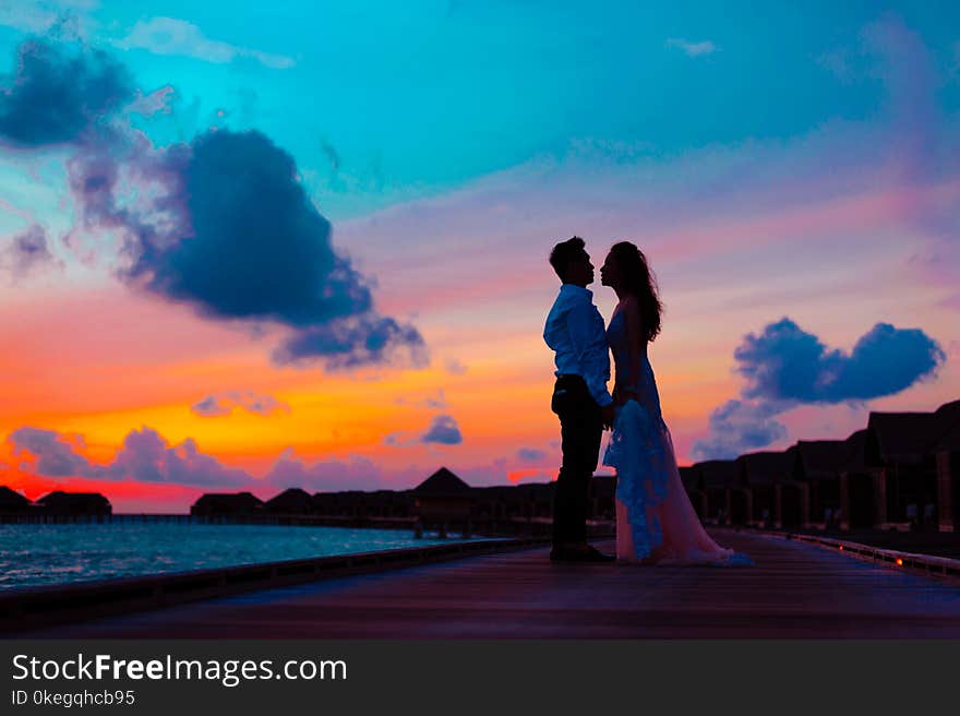 Man and Woman Wearing Wedding Attire Standing on Sea Dock during Golden Hour