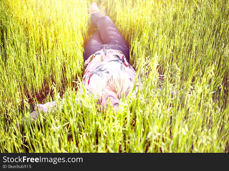 Young woman enjoying the lying on her back on the green grass in the garden.