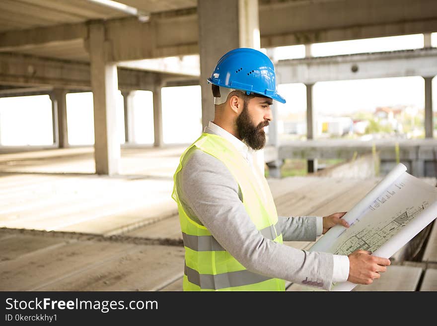 A young man with a beard looks at the construction plans, it is on a building construction site. A young man with a beard looks at the construction plans, it is on a building construction site.