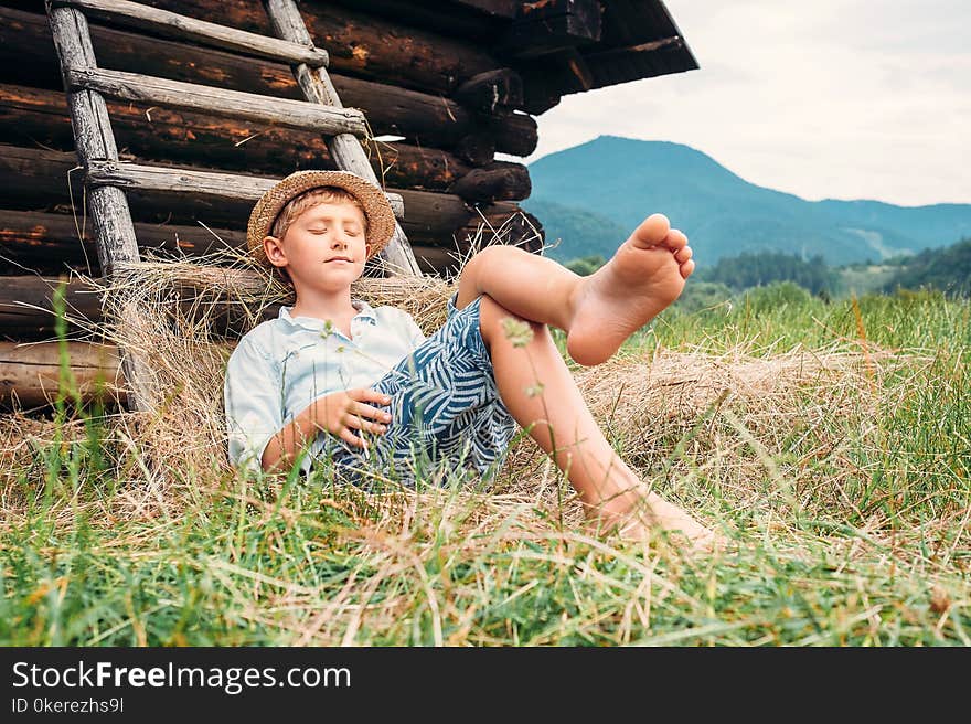 Boy In Straw Hat Lies In Hay Near The Barn