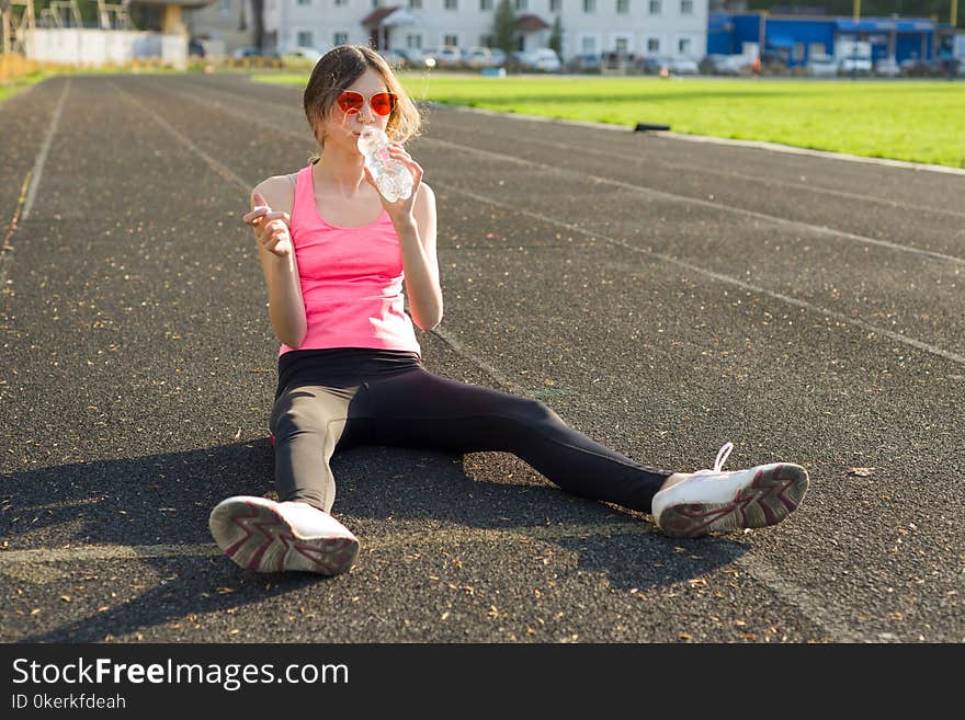 Beautiful teenage girl resting after workout at stadium, girl sat down to relax, drinking water. Beautiful teenage girl resting after workout at stadium, girl sat down to relax, drinking water