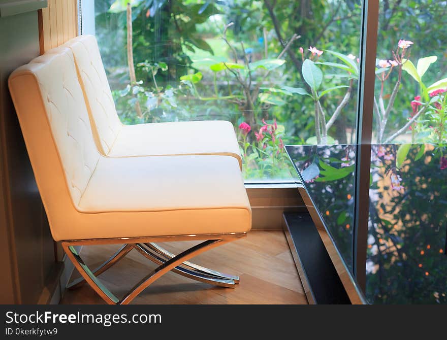 Relaxing moment in the coffee cafe, soft cream leather sofas with the black glass table next to large window with green decorative garden view.