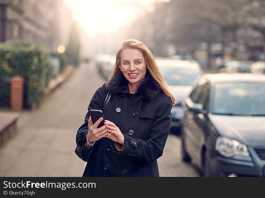 Attractive stylish woman with long blond hair using her mobile in an urban street in a busy town smiling as she reads a text message