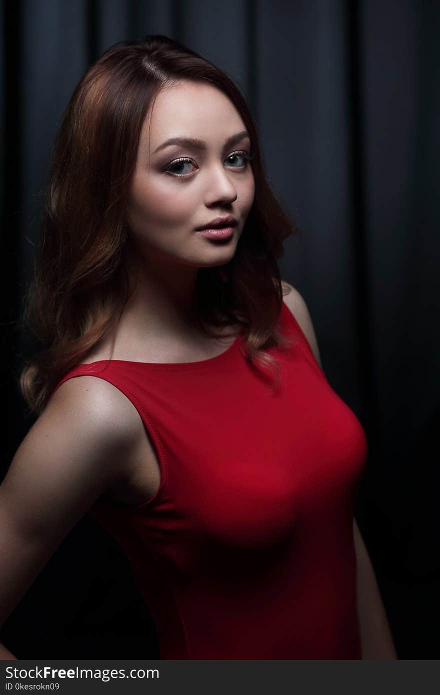 Pretty young model woman with dark hair in an amazing red dress posing in a dark studio. Pretty young model woman with dark hair in an amazing red dress posing in a dark studio