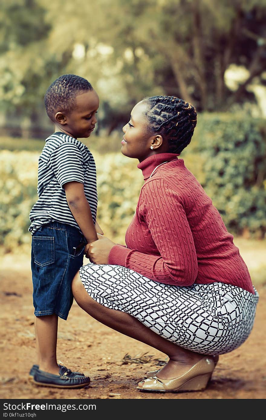 Tilt Shift Lens Photography of Woman Wearing Red Sweater and White Skirt While Holding a Boy Wearing White and Black Crew-neck Shirt and Blue Denim Short