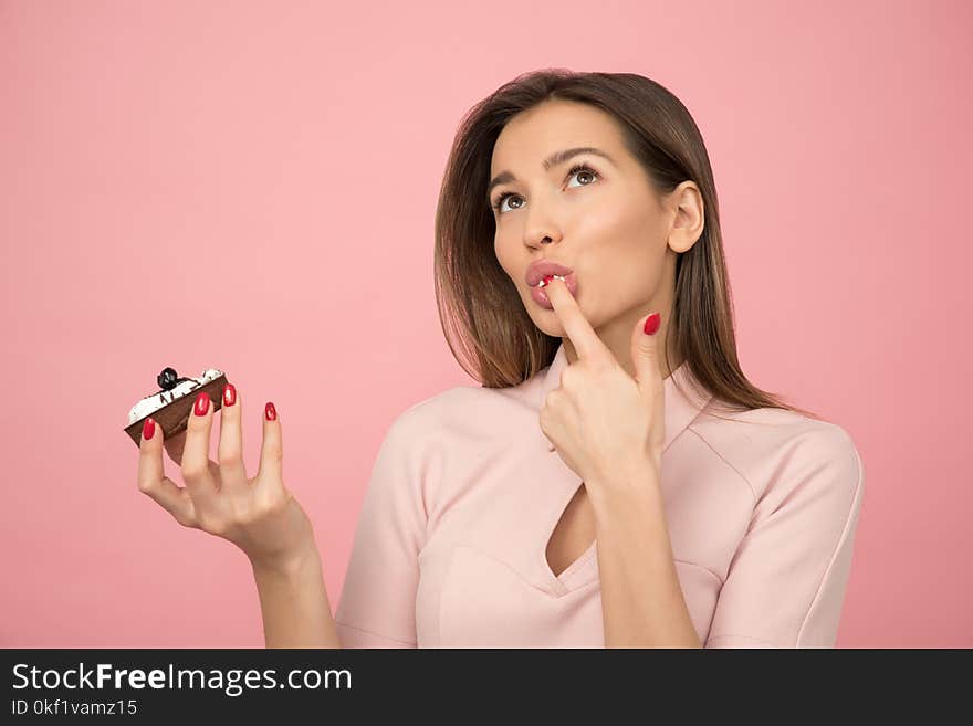 Woman Eating Cupcake While Standing Near Pink Background Inside Room