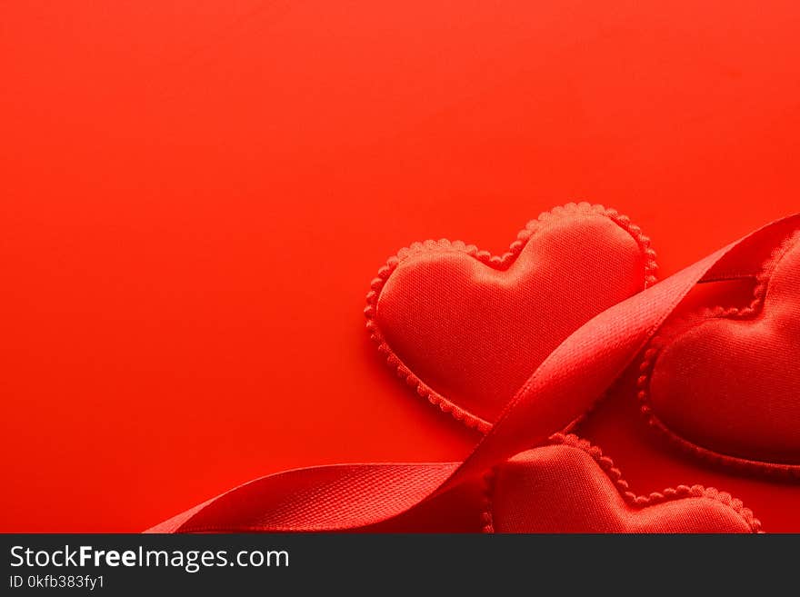 From above small fabric hearts and ribbons on red background. From above small fabric hearts and ribbons on red background.