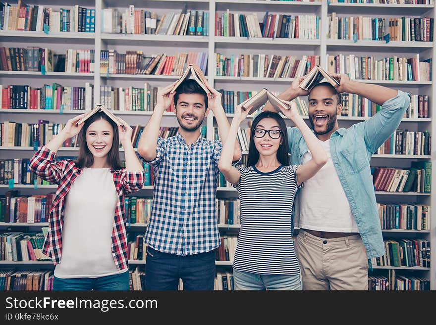 Classmates, international friendship, fun and teenage concept. Group of four cheerful students teenagers in casual outfits with books in the form of a roof over the head fooling around in library