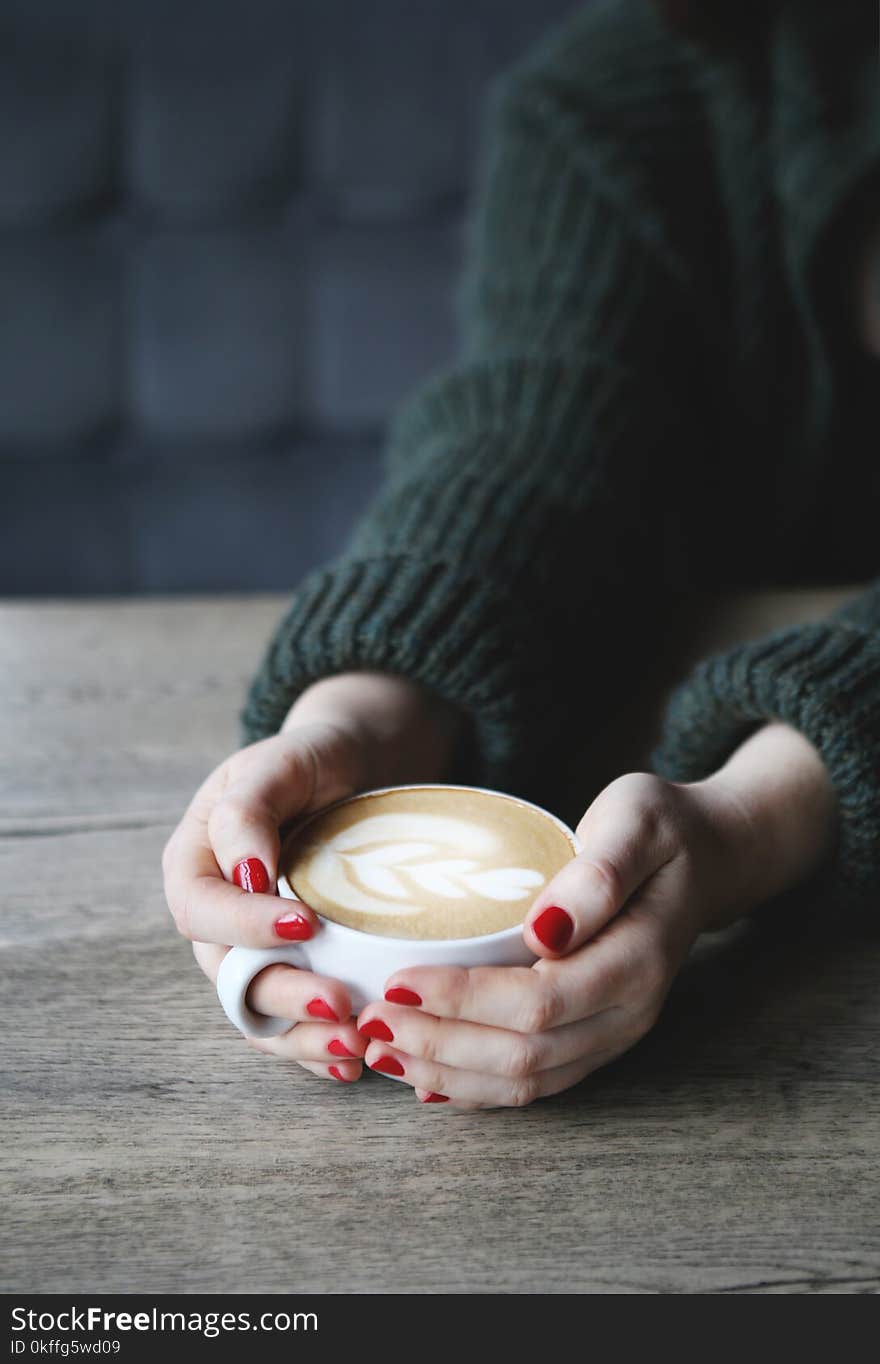 Female hand hold coffee cup with heart shape on wooden table