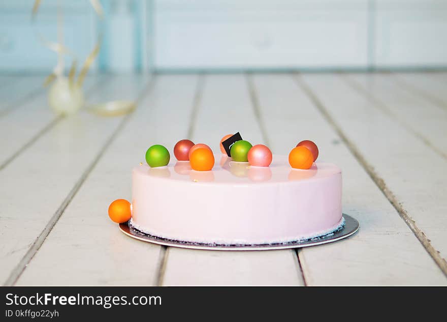 Pink mousse cake with colorful balls on a white wooden floor