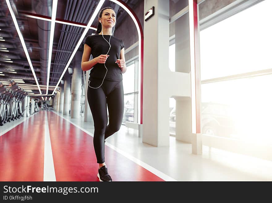 Athletic sporty fit girl with headphones running on run track in gym. Athletic sporty fit girl with headphones running on run track in gym