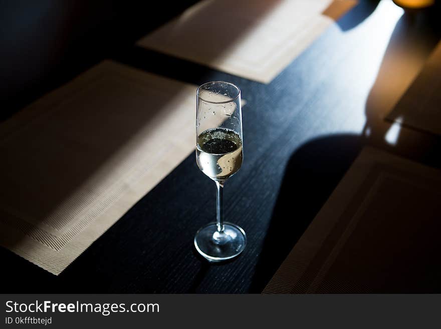 A glass of champagne shitoit on a dark wooden table in the setting sun.