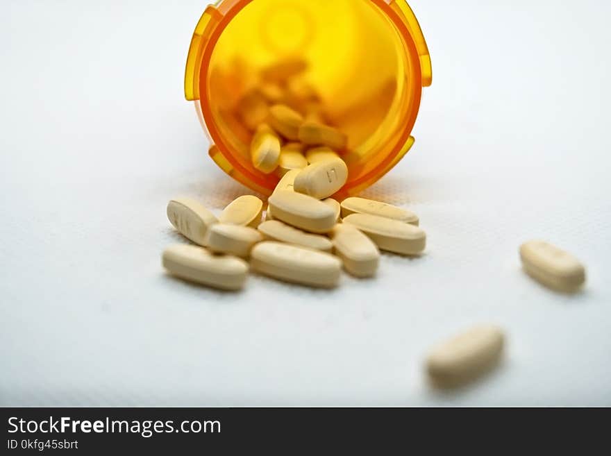 Medicine bottle toppled over with pills spilling out the end onto a table. Medicine bottle toppled over with pills spilling out the end onto a table.