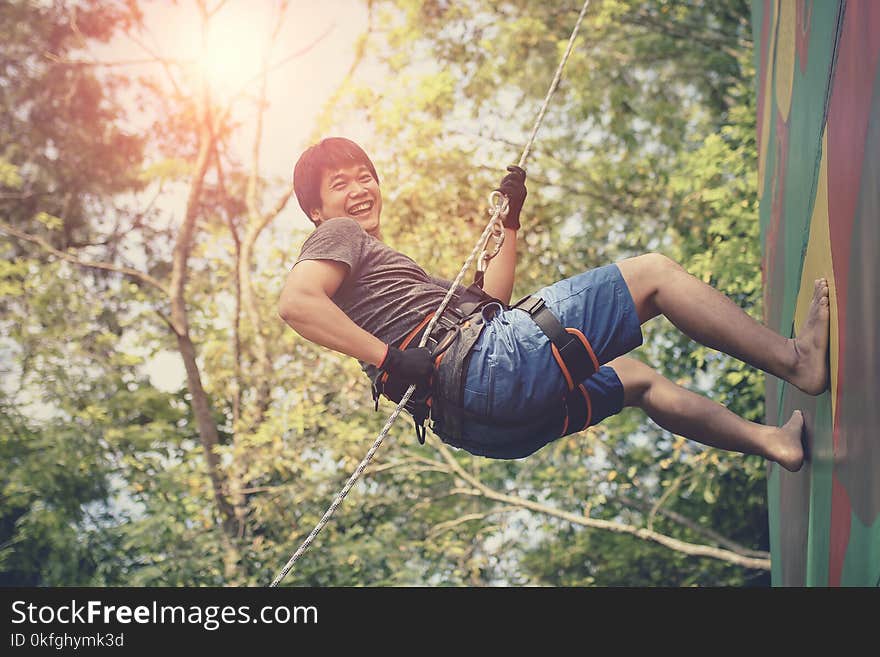 asian younger man hanging on clip hiking safety rope and laughing with happiness emotion