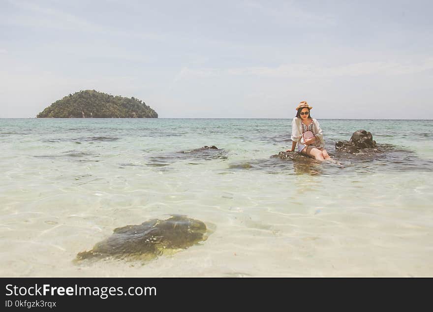 Woman Wearing White Top Sitting on Brown Rock on Body of Water during