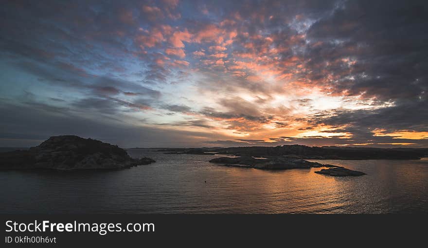 Body of Water Near Mountains Taken Under Orange Clouds during Sunset