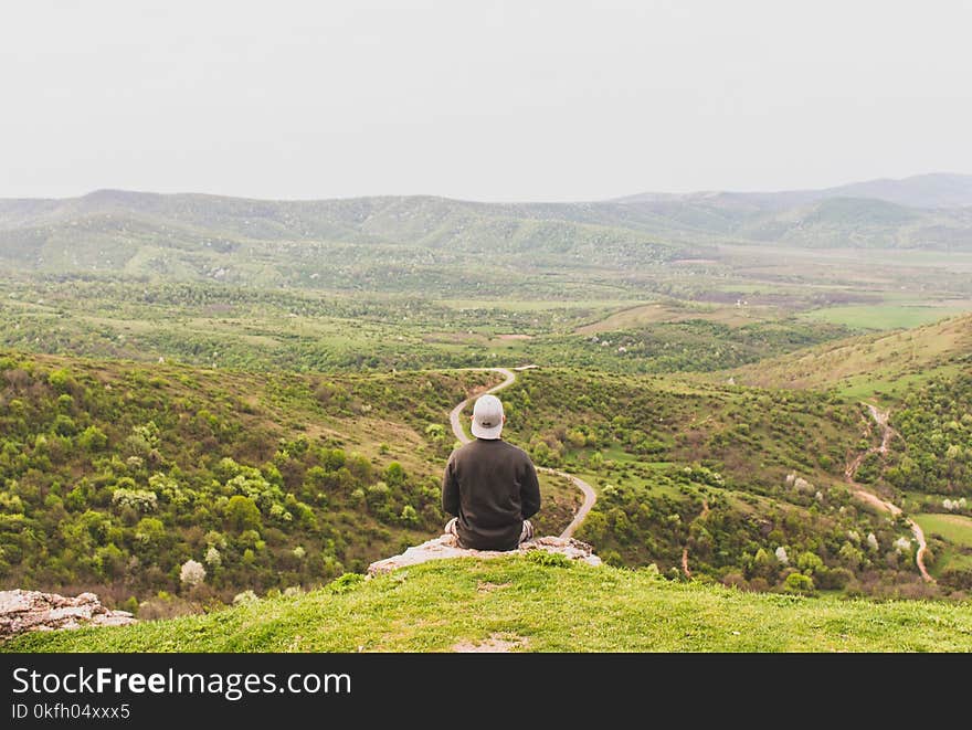 Man Sitting on Mountain Facing Forest Field