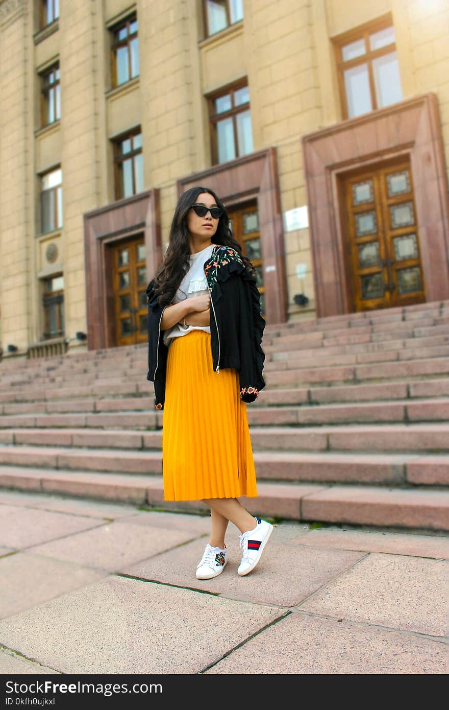 Women Wearing Black Jacket and Pleated Yellow Skirt Standing on Brown Floor