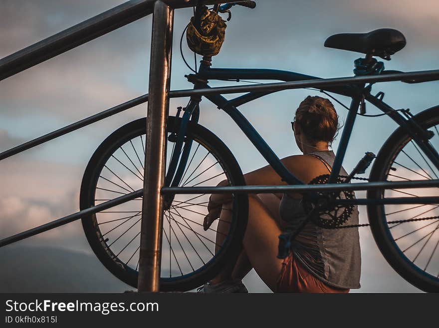 Woman in Gray Tank Top Sitting Beside Black Cruiser Bike