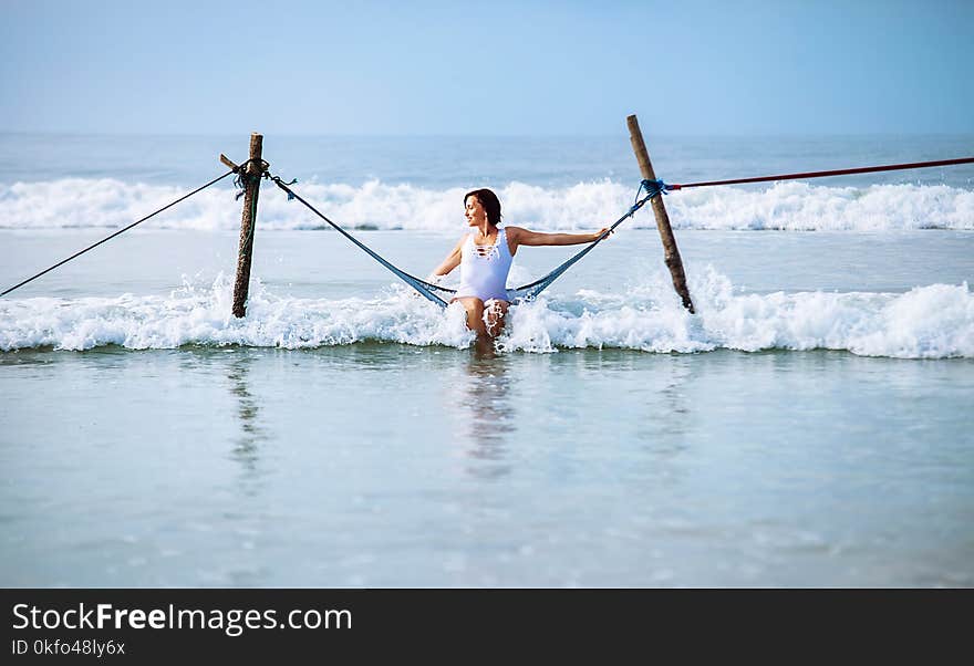 Woman in white swimsuit sits in hammock swing over the ocean surf line