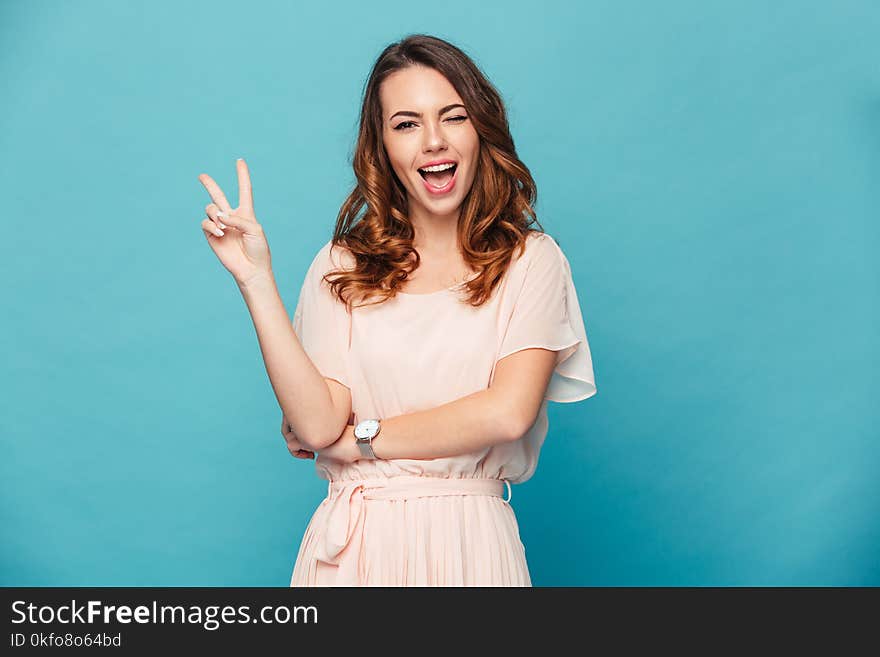 Image of cute young lady standing isolated over blue background. Looking camera showing peace gesture. Image of cute young lady standing isolated over blue background. Looking camera showing peace gesture.