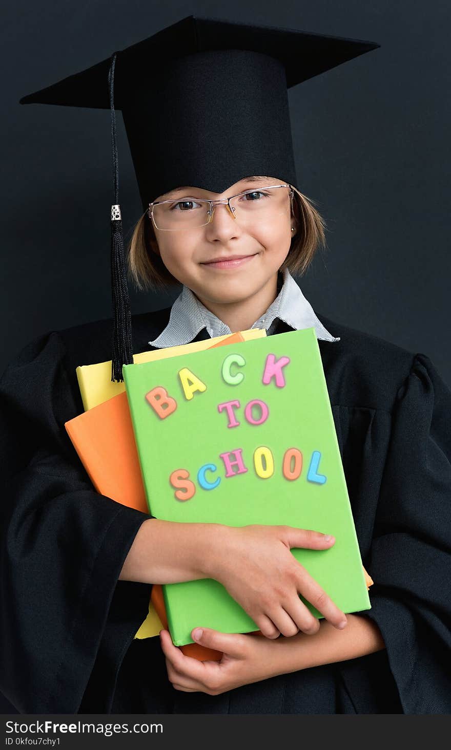 Portrait of graduate little girl student in black graduation gown with hat and books, on white background. Child back to school and educational concept. Portrait of graduate little girl student in black graduation gown with hat and books, on white background. Child back to school and educational concept.