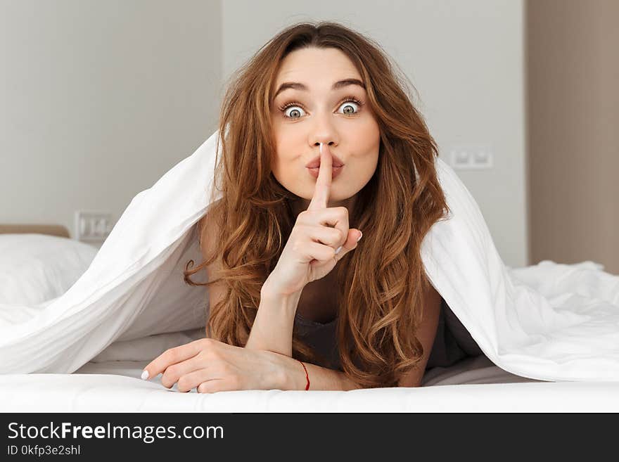 Photo of young brunette woman lying in bed under blanket at home