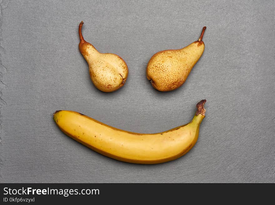 Scary smile made of two pears and banana lying on gray slate background, top view